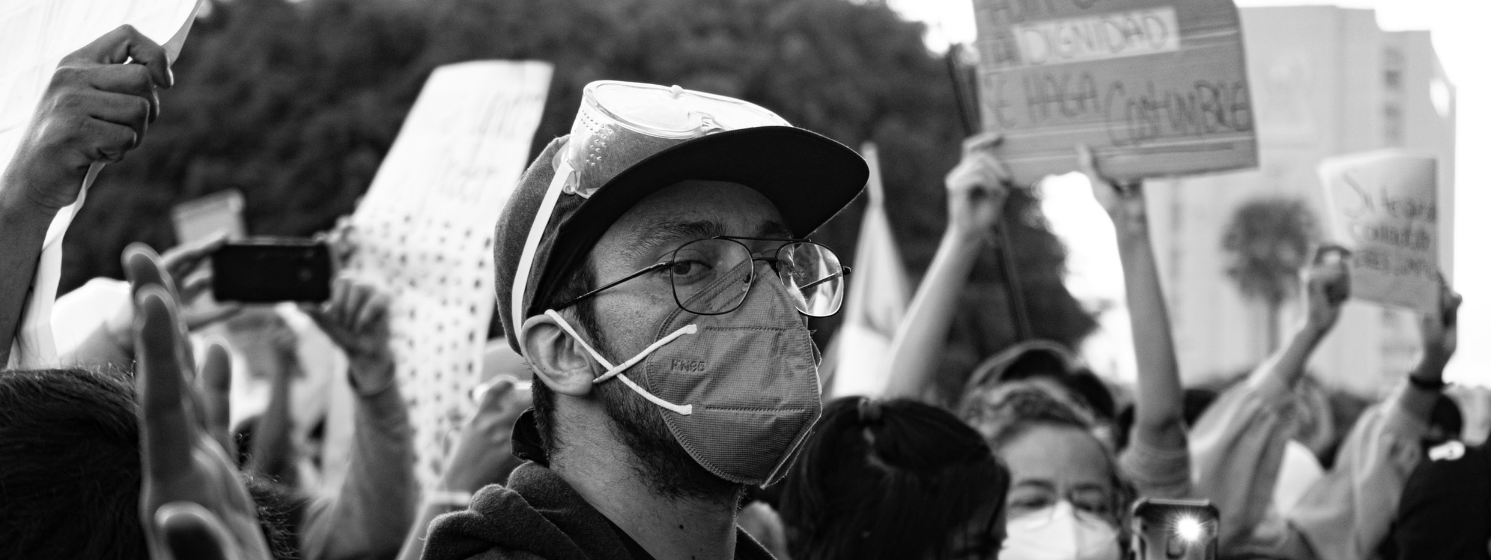 A man wearing a baseball cap and face mask stairs at the camera amid a protest